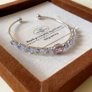 Detailed view of an elegant open cuff bracelet with pink and blue oval zircons in a box