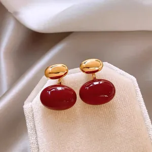 Elegant vintage gold-tone earrings with large oval red stones on a beige velvet stand