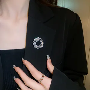 Close-up of sparkling zircon wreath brooch and gold geometric ring on black blazer suit