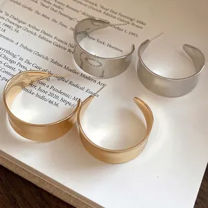 Elegant C-shaped hoop earrings in gold and silver finishes on vintage book background.