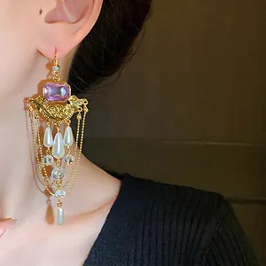 Boucles d'oreilles pendantes de style palais français avec cristaux violets et perles sur modèle.