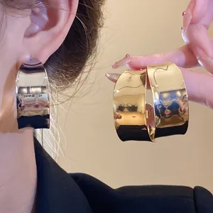 Close-up of wide polished C-shaped hoop earrings in gold and silver finish
