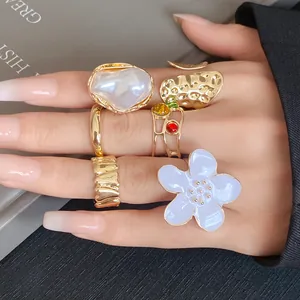 Detail view of gold chunky rings set with blue flower and pearl on a manicured hand.