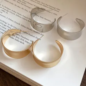 Detail of retro minimalist gold and silver C-shaped hoop earrings with matte and glossy finishes.