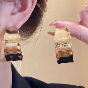 Close-up detail of oversized gold-tone C-shape hoop earrings with smooth polished finish