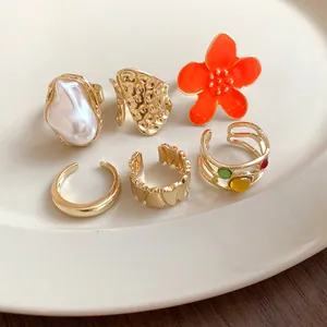 Close-up view of six irregular gold-tone open rings featuring flower and pearl details