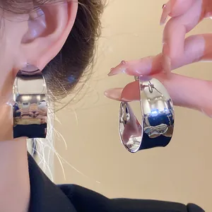 Detailed view of highly reflective silver C-shape hoop earrings showing wearing effect