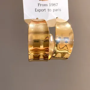 Macro detail of elegant polished gold-finished C-shape hoop earrings in retro style.