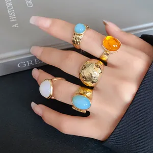 Detailed view of chunky gold-tone metallic rings set with colorful oval stones on hand