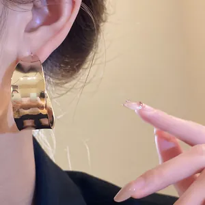 Close-up detail of vintage minimalist gold C-shaped wide hoop earrings worn on a model's ear