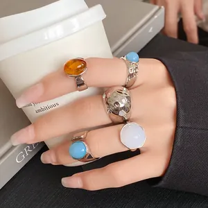 Detail view of irregular metal rings with colorful stone accents on a person's hand