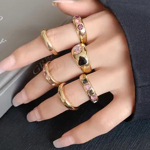 Macro detail of chunky gold geometric rings with pink and black stones on a hand.