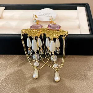 Détail de boucles d'oreilles vintage en or avec gemmes mauves, perles et glands