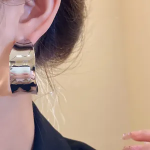 Close-up detail of glossy silver C-shaped hoop earrings on model's ear