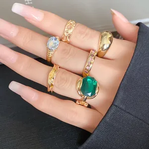 Close-up of an elegant gold ring set with vibrant green and blue gemstones on a hand