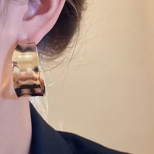 Detailed view of a chunky gold-toned C-shaped hoop earring on a model for a chic look