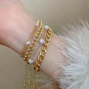Vue détaillée de bracelets dorés superposés avec chaînes serpent, perles et gourmettes.