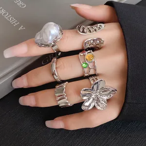 A set of silver-toned irregular metal rings with floral and pearl accents worn on hand