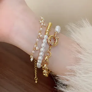 Gros plan de bracelets dorés vintage superposés avec perles et fermoir en T rétro détaillé.
