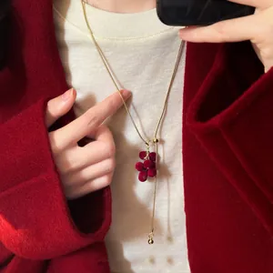 Close-up of a gold adjustable necklace with red flocked grape cluster pendant on coat.
