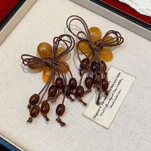 Dettaglio di orecchini a fiore in resina gialla con fiocco marrone e nappe di perline