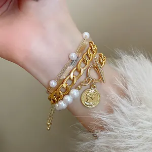 Détail d'un bracelet doré multicouche avec perles, chaîne serpent et pendentif pièce