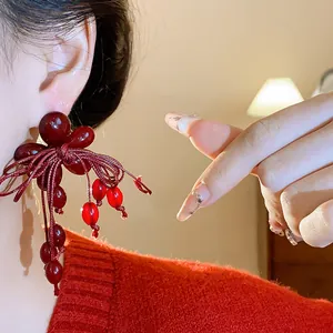 Dettaglio orecchini eleganti in resina rossa a fiore con fiocco e nappine per autunno.