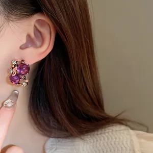Dettaglio di orecchini vintage con fiori viola e foglie indossati da una modella.