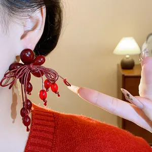 Primo piano di orecchini rossi con fiori, fiocchi e nappe indossati sull'orecchio.