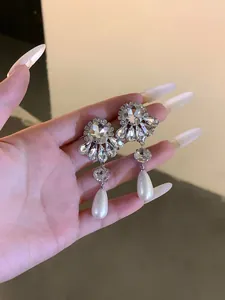 Detailed view of silver needle rhinestone flower earrings with white waterdrop pearls
