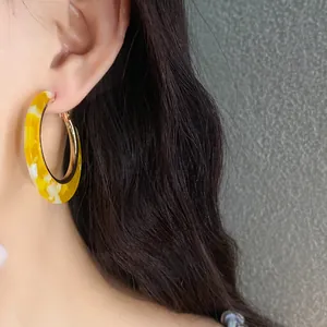 Close-up detail of a marbled yellow acetate hoop earring worn on a model's ear