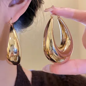Grandes boucles d'oreilles goutte d'eau dorées montrées sur l'oreille et à la main, style chic