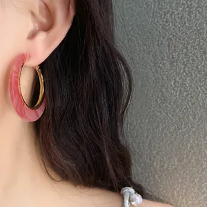 Detail view of a vintage pink marbled acetate hoop earring worn on a female ear