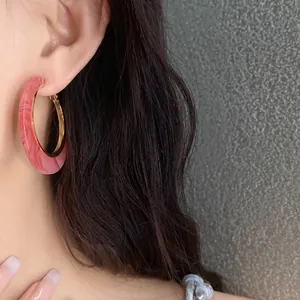 Close-up of pink marbled acetate hoop earrings with gold inner rim worn on ear.