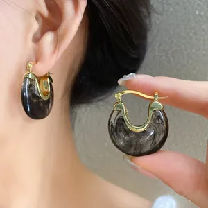 Detailed view of resin hoop earrings with dark smoke marble texture and gold finish