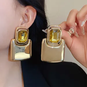 Detail shot of heavy gold-tone metal earrings with large yellow emerald-cut crystals