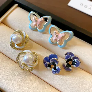 Close-up of mixed stud earrings featuring butterflies, pearls, and purple flowers