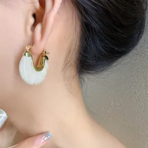Elegant detail showing a gold-plated white resin hoop earring worn on a woman's ear.