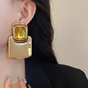 Detailed close-up of oversized square gold stud earrings with a yellow crystal on model