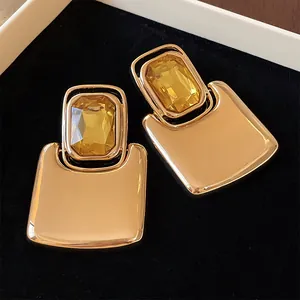 Close-up detail of chunky gold-toned earrings featuring large faceted yellow crystal centerpieces