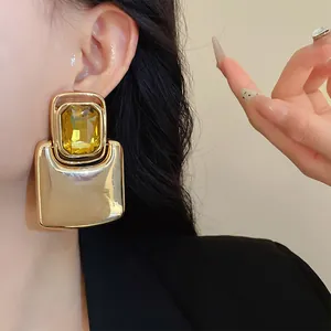 Close-up of oversized square metallic earrings featuring a large yellow gemstone on model.