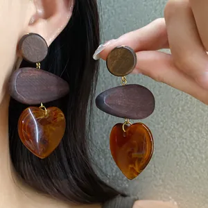 Close-up of ethnic style wooden heart drop earrings with amber-like acrylic texture