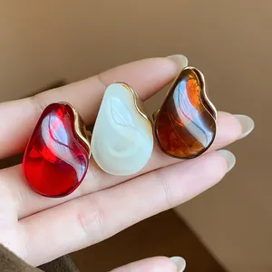 Close-up detail of teardrop resin open rings in red, pearl white and amber brown colors