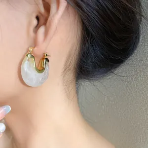 Detail view of golden hoop earring with white marbled resin inlay worn on ear