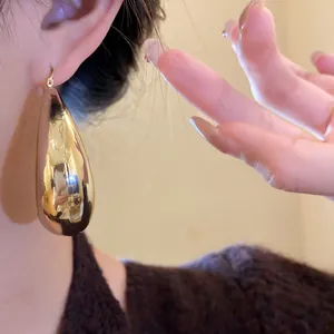 Gros plan sur une grande boucle d'oreille goutte d'eau dorée portée par un modèle élégant