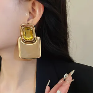 Close-up of oversized square metal earrings with a large yellow crystal on model ear.