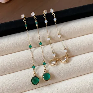 Dettaglio di orecchini pendenti lunghi in argento con gemme di vetro tonde verdi e chiare.