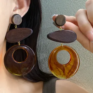 Close-up of geometric earrings with dark wood studs and amber acrylic rings.