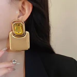 Close-up of exaggerated square gold metal stud earrings with a vibrant yellow gemstone