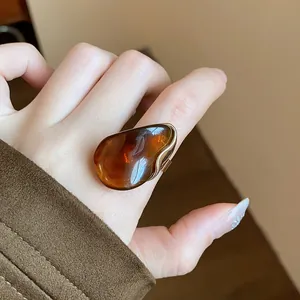 A detailed close-up shot of a stylish amber resin oval open ring worn on a finger